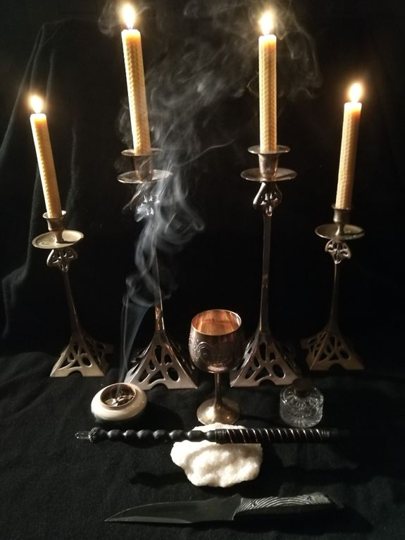 Candles and Chalice A ritual altar setup with four lit beeswax candles in metal holders, an incense burner, a chalice, a ceremonial dagger, and a wand