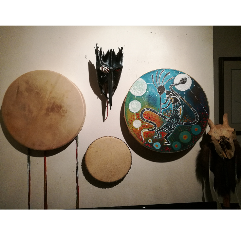 Drums and Mask A wall display featuring three ceremonial drums, including a hand-painted shamanic drum with a Kokopelli design, and a leather ritual mask